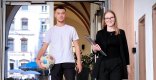 Ein junger Mann in Sportkleidung mit Fußball und eine junge Frau in Businesskleidung mit Tablet gehen gemeinsam aus dem Verwaltungsgebäude.