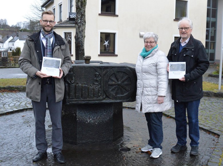 Bild zeigt Bürgermeister Ulrich Richter-Hopprich als Herausgeber und die Autoren Eleonore Lenz und Winfried Röther am Dorfbrunnen in Niederelbert
