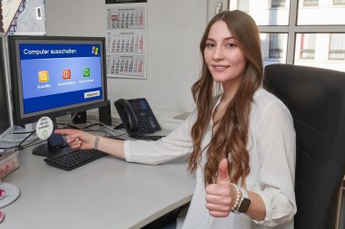Die Auszubildende Sandra Schäfer sitz am Computer und zeigt auf einen Aufkleber am Arbeitsplatz.