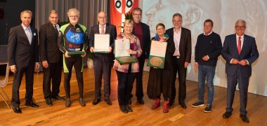 Staatsminister Roger Lewentz und die verantwortlichen Vertreter der Kommunen mit den Geehrten, die ihre Plakette präsentieren.