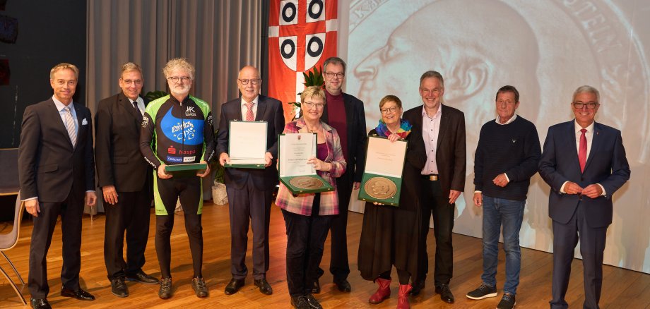 Staatsminister Roger Lewentz und die verantwortlichen Vertreter der Kommunen mit den Geehrten, die ihre Plakette präsentieren.