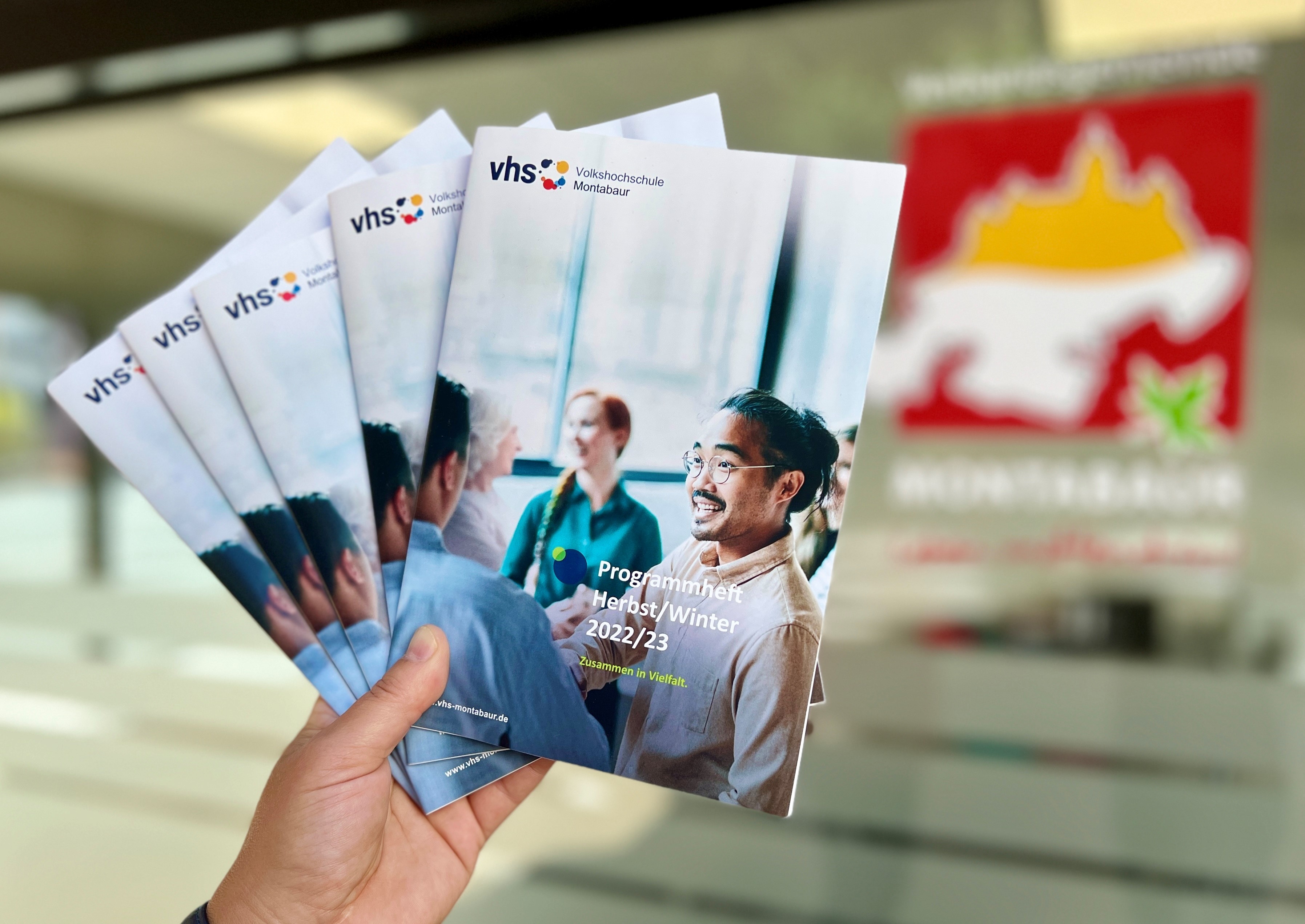 Eine Hand hält die neuen vhs-Programme hoch.