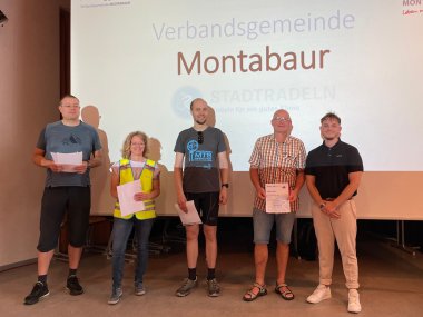 Bürgerinnen und Bürger stehen mit ihren Siegerurkunden vor einer Leinwand mit der Aufschrift "Verbandsgemeinde Montabaur".