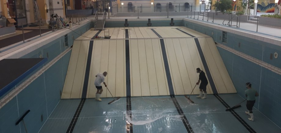 Bild zeigt leeres Schwimmbecken mit Menschen die Reinigungsarbeiten durchführen