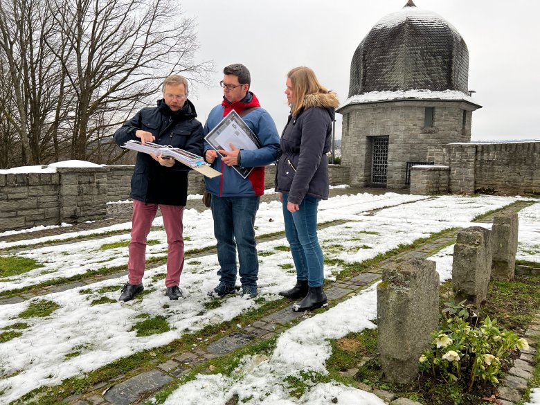 Claus Peter Beuttenmüller, Markus Kuch und Lisa Gerharz stehen im Ehrenhain und studieren die Aufzeichnungen von Claus Peter Beuttenmüller.