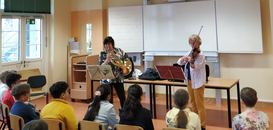 Bild zeigt zwei Musikerinnen vor einer Schulklasse