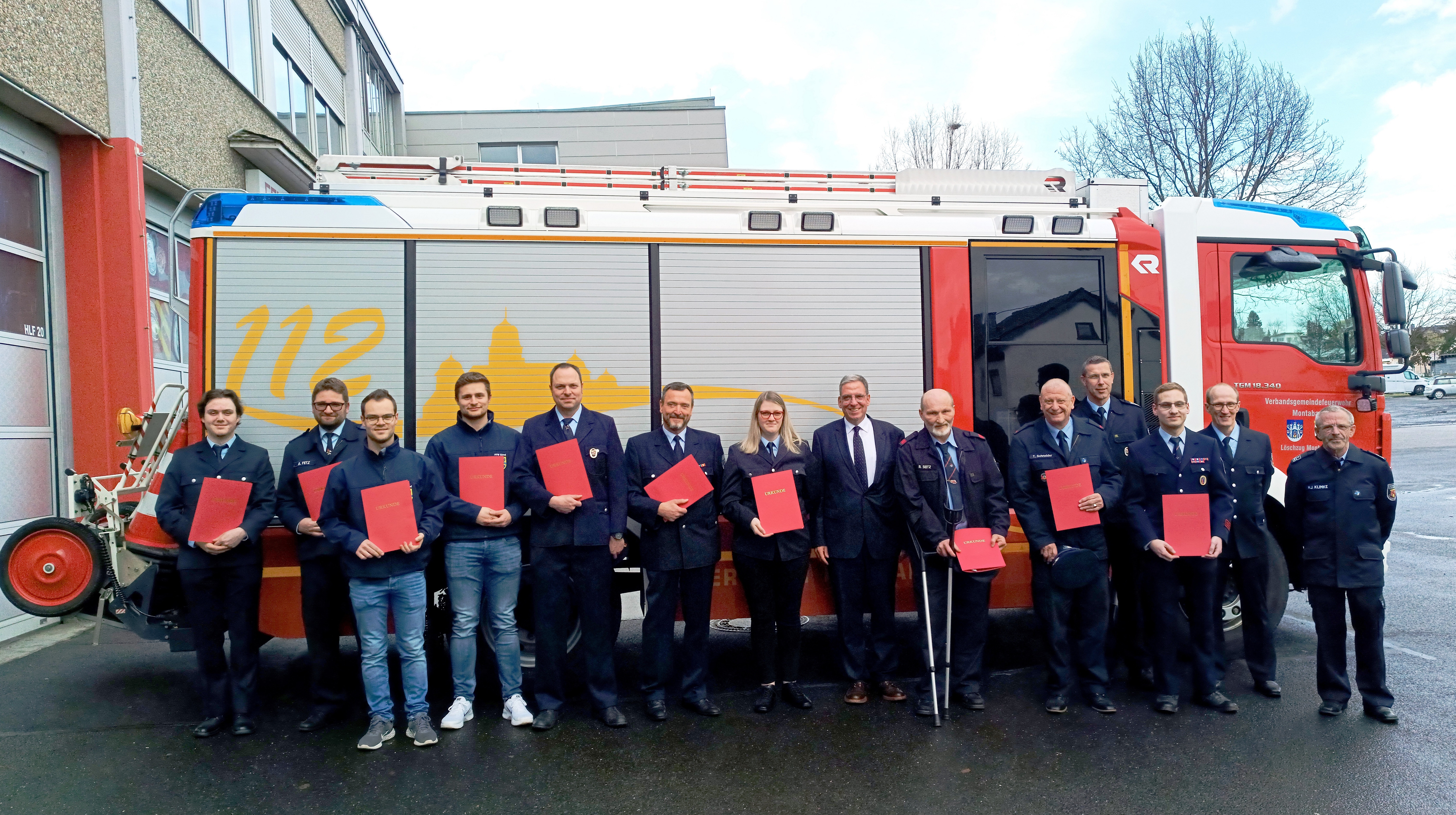 Die beförderten Feuerwehrleute stehen mit ihren Urkunden vor einem Feuerwehrauto.