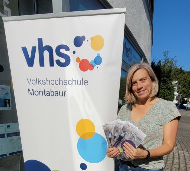 Frau mit Programmheften vor dem Roll-up der vhs