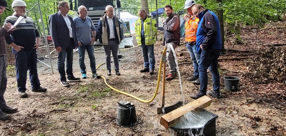 Die Verantwortlichen stehen im Wald um den Bereich, wo die Probebohrung stattfand. Wasser sickert aus dme Boden.  