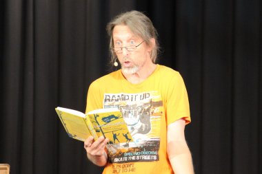 Mann mit orangenem Shirt und Brille liest aus einem Buch
