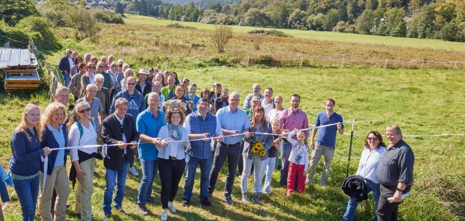 Menschen stehen auf einer grünen Wiese vor einem weißen Band