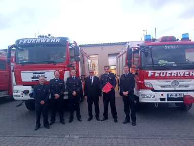 Der wiedergewählte Wehrführer Henrik Mansel  und alle Verantwortlichen vor zwei Feuerwehrfahrzeugen.