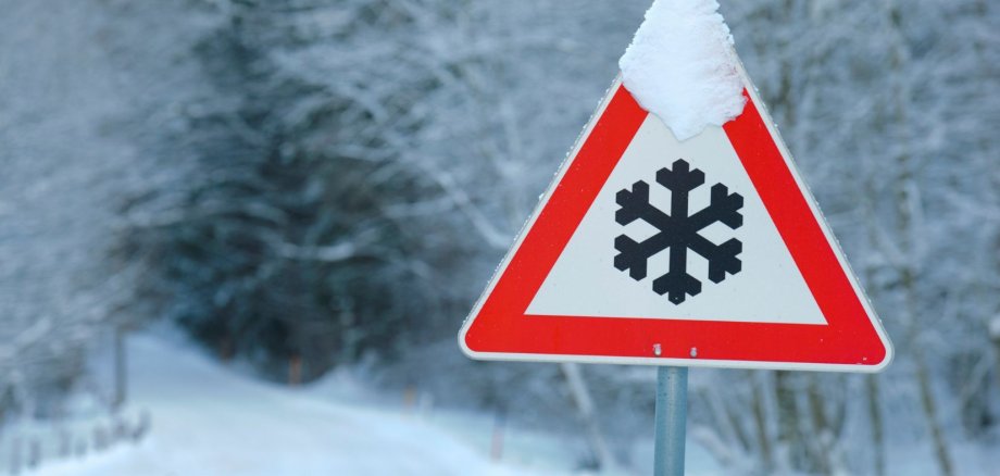 Ein Warnschild "Schnee" in einer Winterlandschaft.