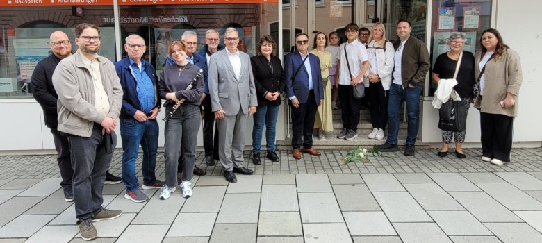 Eine große gemischte Gruppe von Menschen steht für ein Gruppenfoto vor einem Gebäude mit der Aufschrift „V+V Westerwald“, einige halten Blumen.