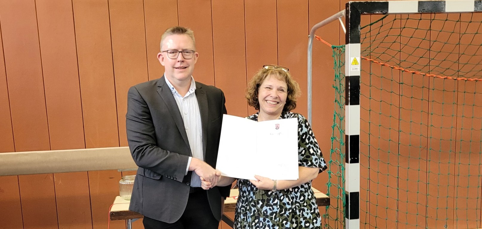 Zwei Personen in einer Turnhalle, eine erhält eine Entlassungsurkunde