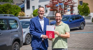 Minister Ebling überreicht Förderbescheid an Beigeordneten Andreas Egenolf. Foto vor Wohnhäusern.