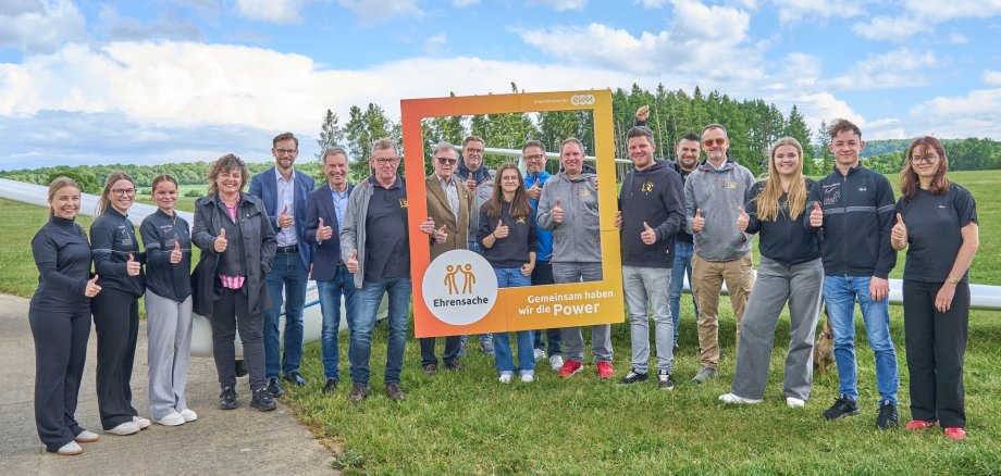 Mehrere Menschen stehen auf dem Flugplatz Montabaur zusammen, während Norbert Rausch von der evm und VG-Bürgermeister Ulrich Richter-Hopprich eine Spende an die Vertreter von vier Vereinen überreichen. Stadtbürgermeisterin Melanie Leicher und Ortsbürgermeister Tobias Reusch aus Nentershausen sind ebenfalls Teil der Gruppe.