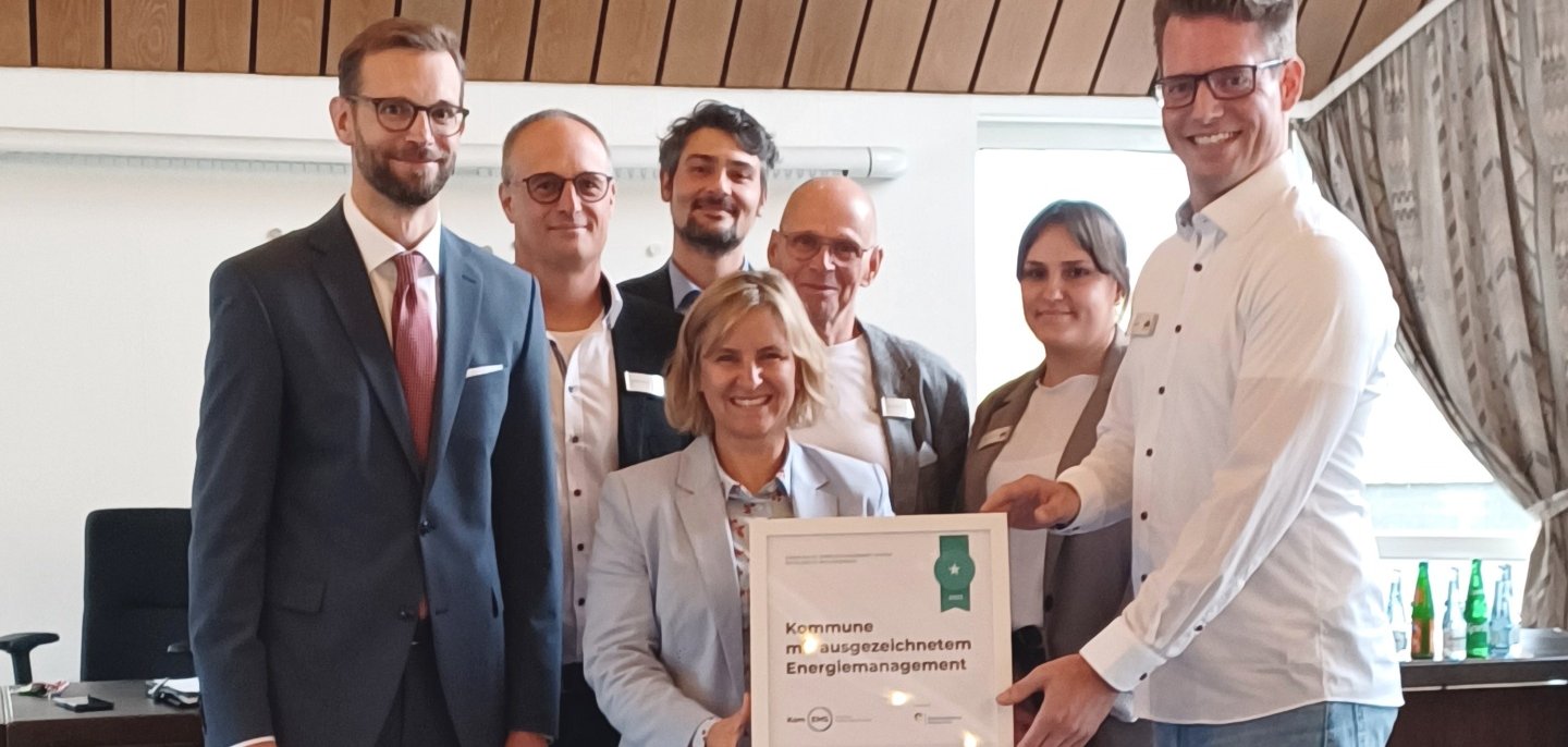 Gruppenfoto mit Klimaschutzministerin Katrin Eder, Bürgermeister Ulrich Richter-Hopprich und dem Energieteam der Verbandsgemeinde Montabaur, die gemeinsam das gerahmte Kom.EMS-Zertifikat präsentieren.