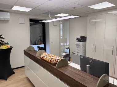 Empfangsbereich der neuen LandarztPlus-Praxis in Welschneudorf mit moderner Theke, Bildschirm, Plexiglasschutz und dekorativem Präsentkorb.