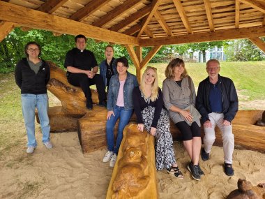 Gruppenfoto von Erwachsenen unter dem neuen Holzpavillon in der Kita St. Martin – darunter die Bildhauerin, Erzieherinnen, Gemeindevertreter und ein Geistlicher.