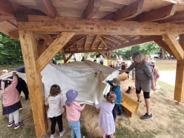 Kinder und Erwachsene ziehen gemeinsam eine Plane vom neuen Holz-Kunstwerk in der Kita, um es feierlich zu enthüllen.