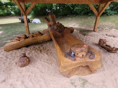 Detailaufnahme des Holz-Kunstwerks „Bärenbande“: Eine große geschnitzte Baumstamm-Skulptur mit verschiedenen Bärenfiguren im Sandspielbereich der Kita.