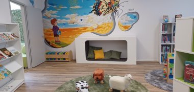 Niedrige Regale in „Kinderhöhe“, Sitzhocker, kleine Tische, Teppiche, Kissen, Sofas und Sitztiere sowie eine Kuschelhöhle machen den Bereich zu einem Paradies für Kinder.