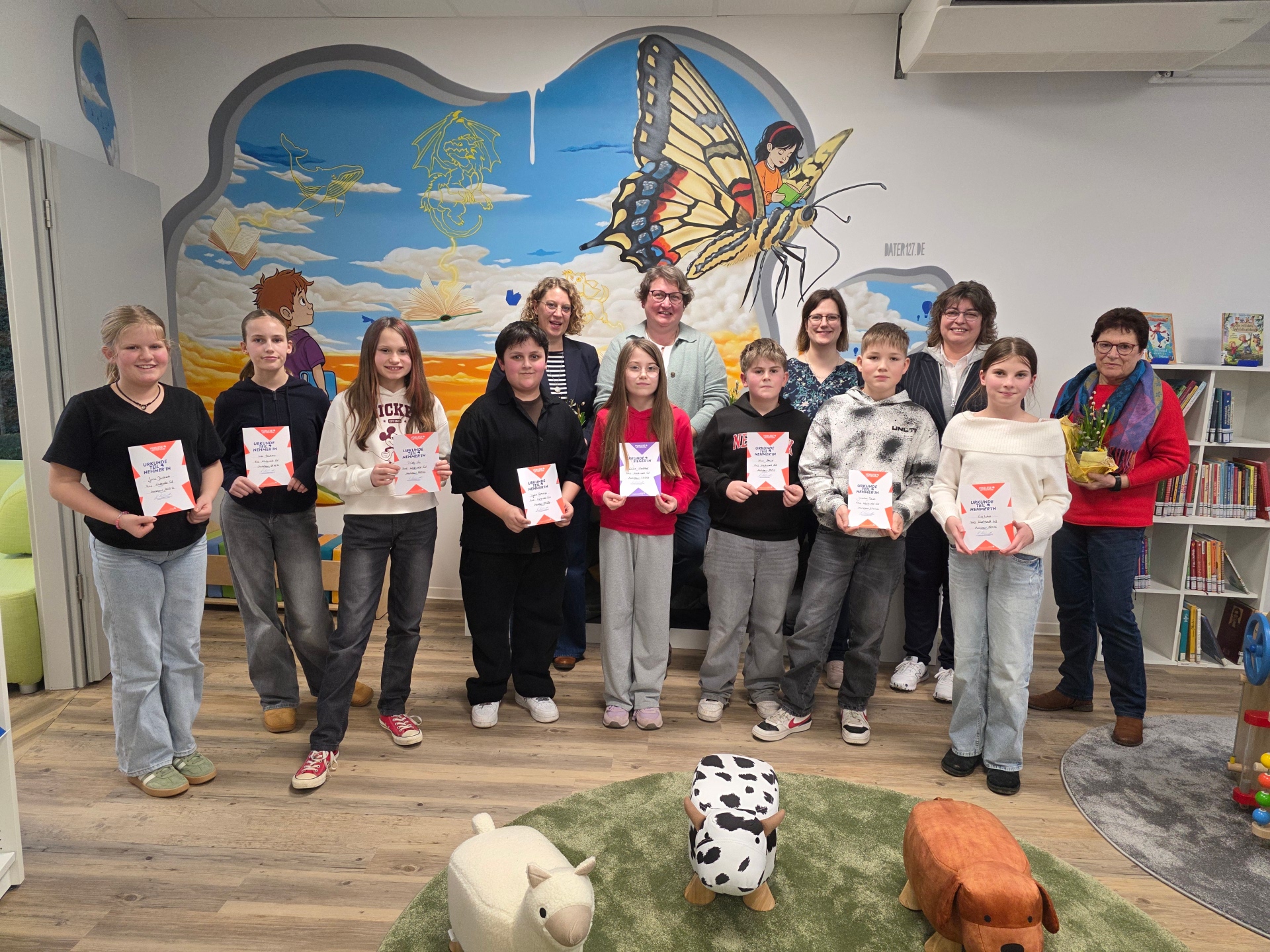 Strahlende Gesichter beim Kreisentscheid Westerwald Süd des Vorlesewettbewerbs in der Stadtbibliothek Montabaur: Die teilnehmenden Schülerinnen und Schüler präsentieren gemeinsam mit der Jury sowie Stadtbürgermeisterin Melanie Leicher und Bibliotheksleiterin Carina Senko stolz ihre Urkunden.