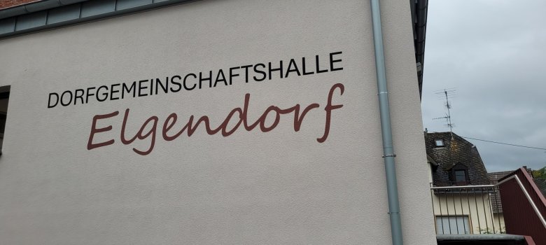 Schriftzug „Dorfgemeinschaftshalle Elgendorf“ an der Außenwand des Gebäudes.
