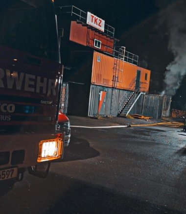 Nächtliche Ansicht der mehrstöckigen Übungsanlage des Technischen Kompetenzzentrums mit Rauchentwicklung. Links im Bild steht ein Feuerwehrfahrzeug.