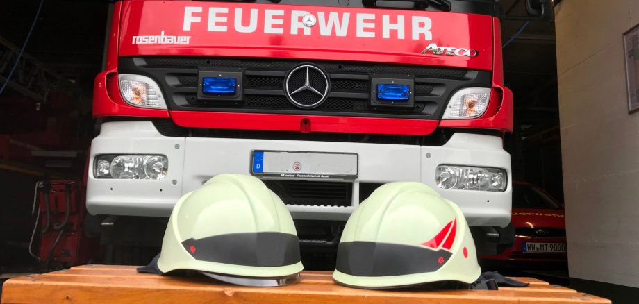 Das Bild zeigt ein Feuerwehrfahrzeug und Feuerwehrhelme.