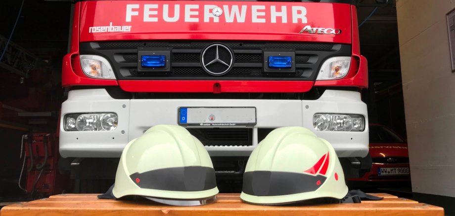 Das Bild zeigt ein Feuerwehrfahrzeug und Feuerwehrhelme